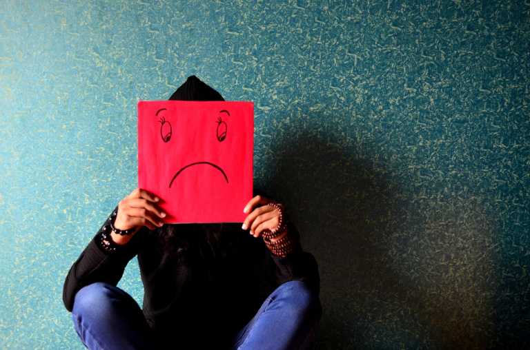 man holding a sad face placard; how to overcome debt fatigue